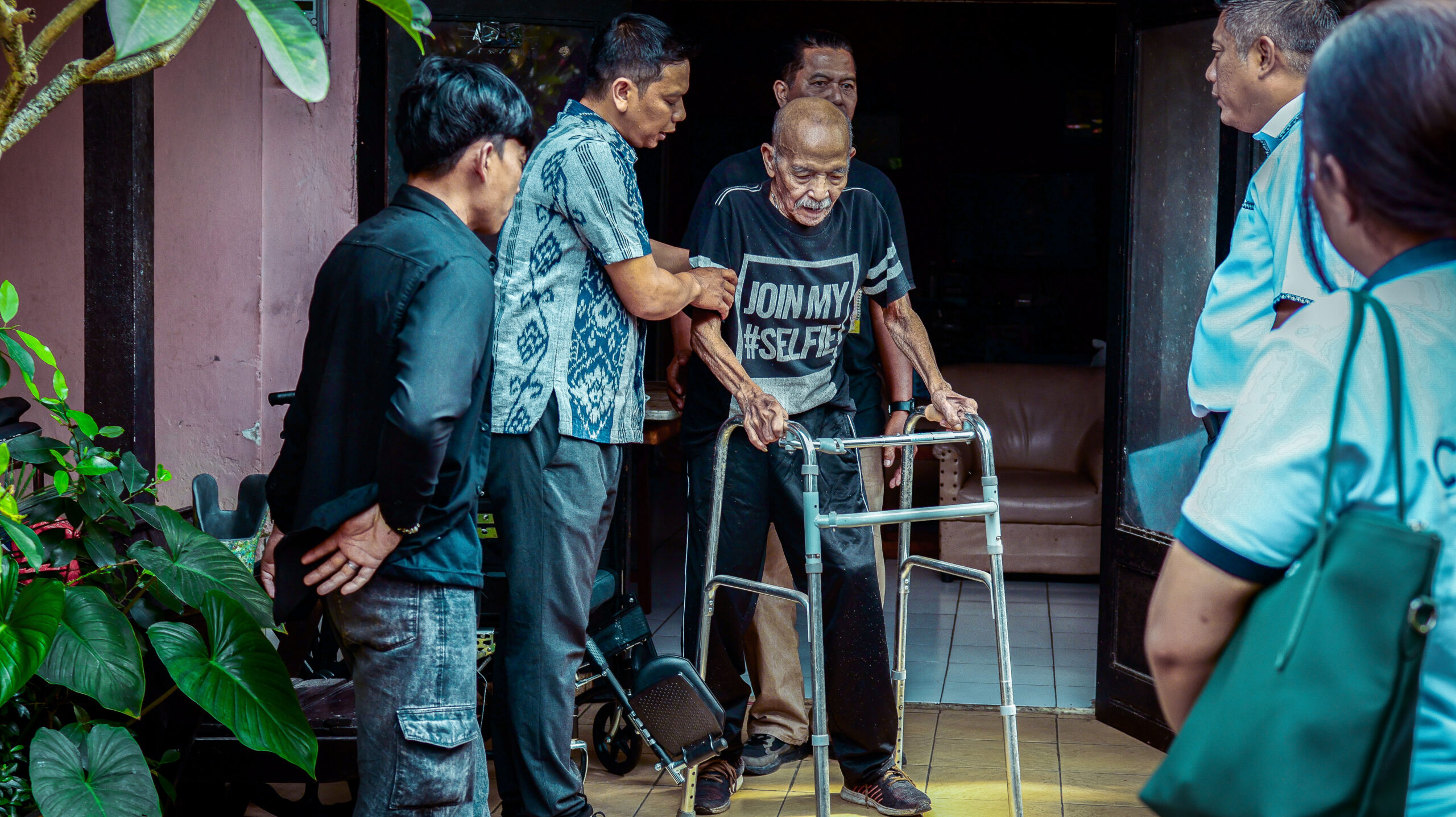An elderly beneficiary using a walker with assistance during a recycled plastic prosthetic leg mobility demonstration.